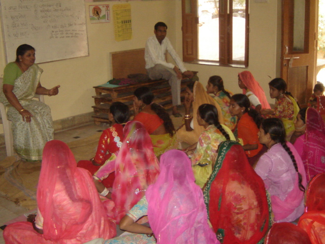 A trainer addressing women in a classroom with a board listing child marriage and other social issues