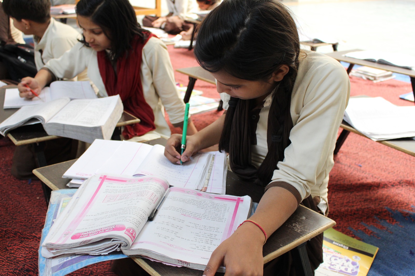 Schoolgirls reading and writing at their classroom desks