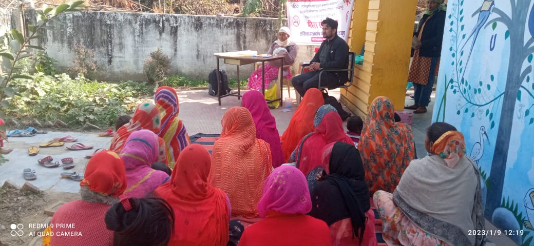 A field worker speaking with women seated in a courtyard